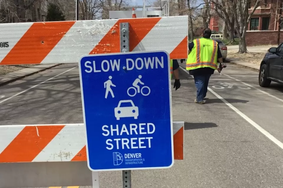 Close-up of blue "Slow Down - Shared Street" sign on orange and white barricade in Denver, Colorado.
